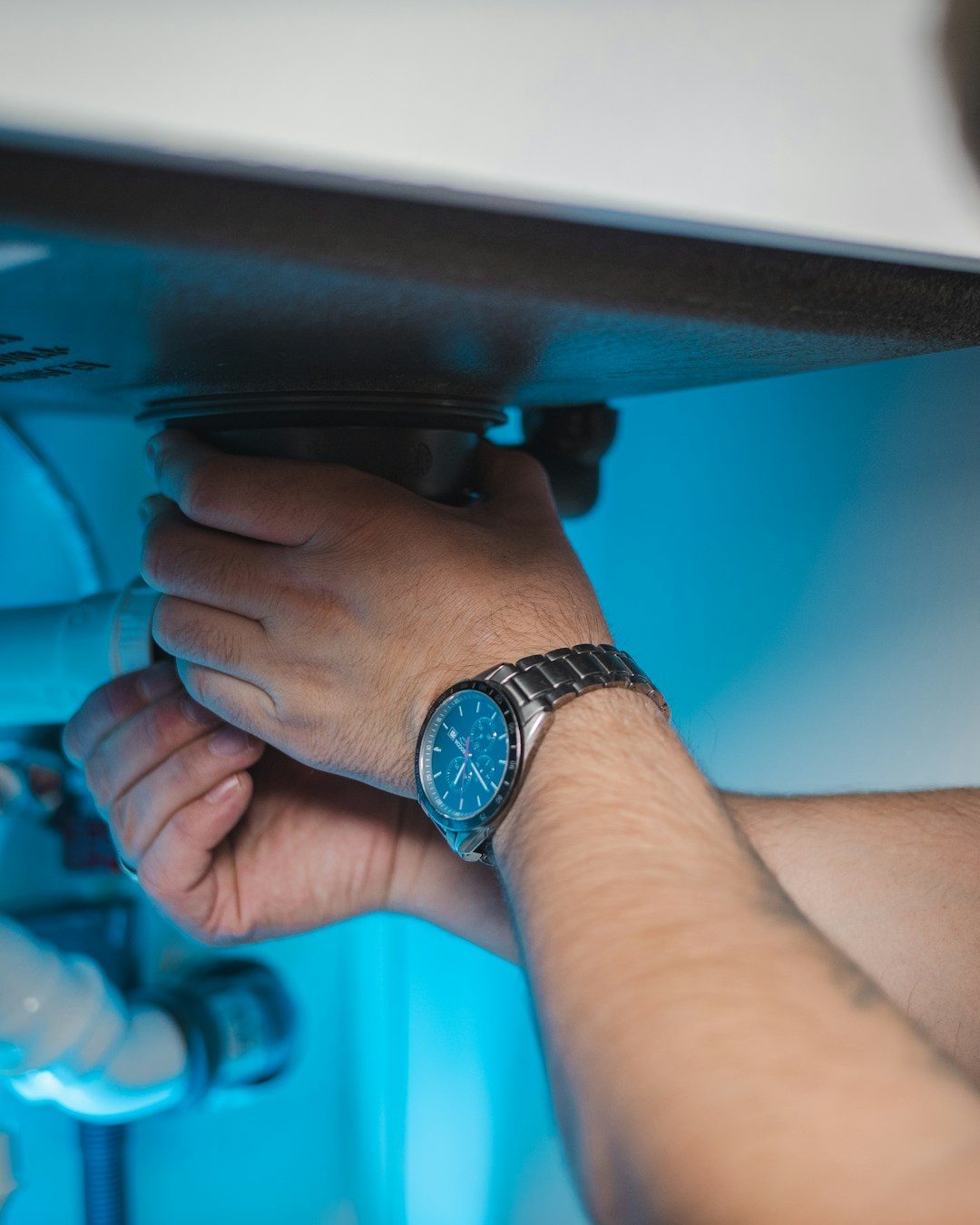 Plumber's hands adjusting pipework and valves beneath a sink